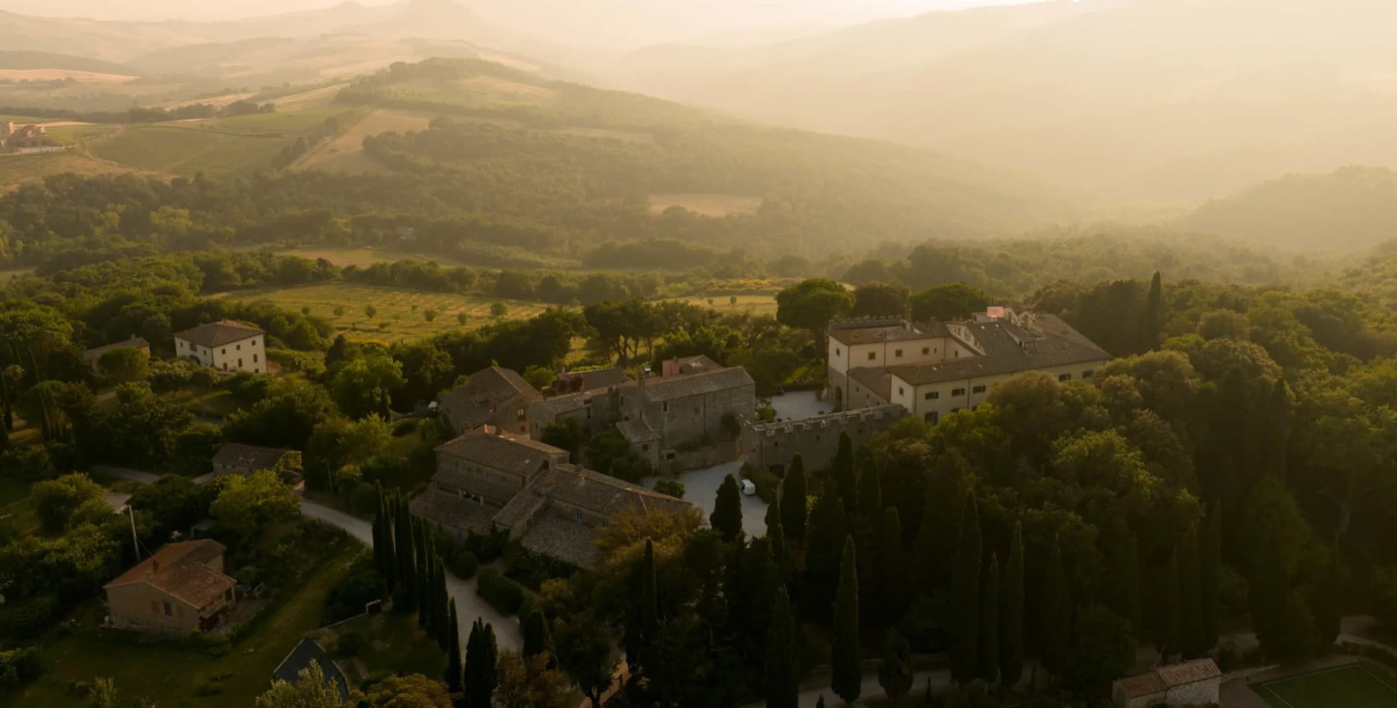 A stone farmhouse among cypress trees in rolling hills at sunrise