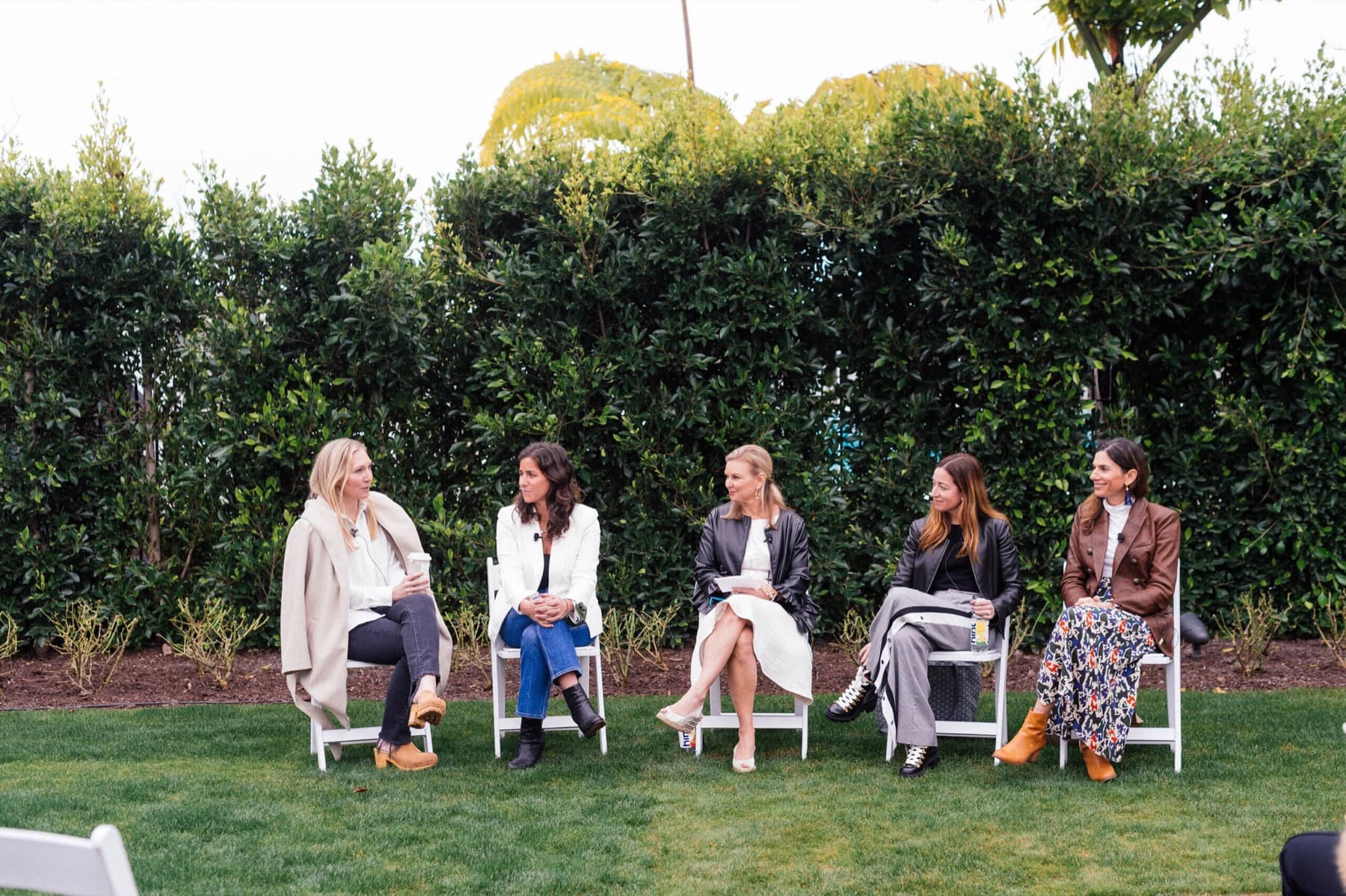 Five travel advisors sitting in a row on white chairs on a lawn