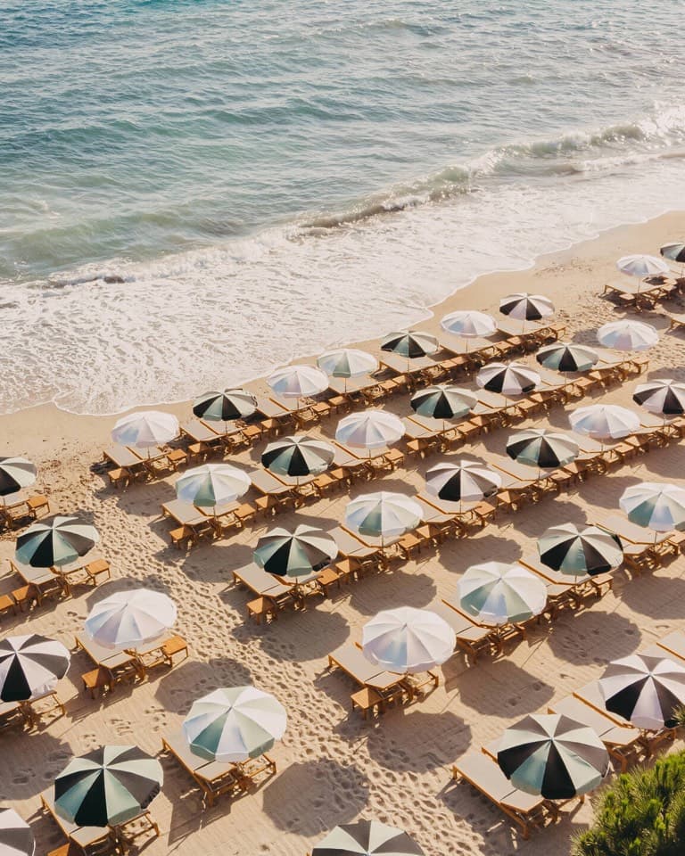 Striped beach umbrellas on a sandy shore from above